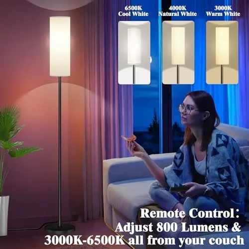 The lamp glowing softly beside a sofa while a person adjusts it with the remote