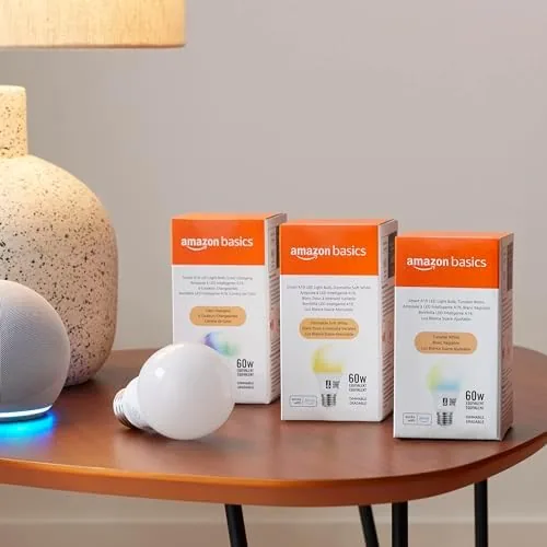 A desk lamp fitted with the smart bulb next to a phone showing the control app