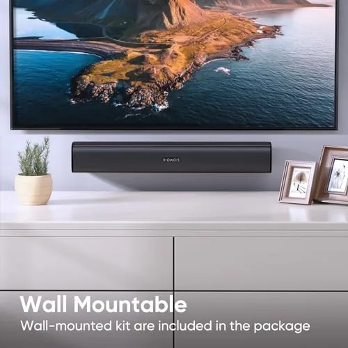 The sound bar mounted on a wall beneath a TV in a tidy bedroom setup