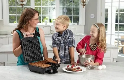 The waffle maker on a counter showing its size next to a toaster