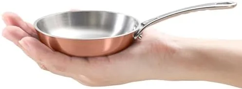 The Macevia mini sauce pan resting on a counter with its copper exterior showing