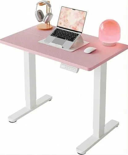 The HUANUO pink standing desk set up in a small apartment corner with a monitor on top